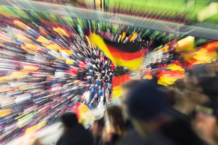 Téléchargez les photos : Image avec appareil photo fait effet de zoom des personnes avec des drapeaux nationaux allemands lors d'un match de football dans le stade - en image libre de droit