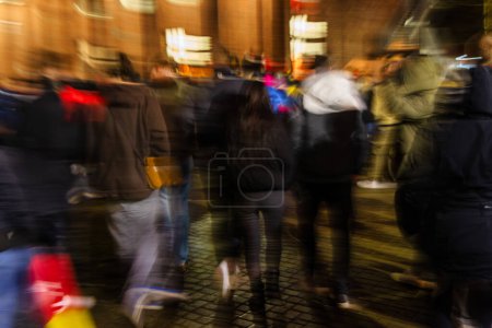 Téléchargez les photos : Photo avec caméra fait flou de mouvement d'une foule de jeunes gens marchant dans la ville pluvieuse la nuit - en image libre de droit