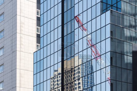 Téléchargez les photos : Image d'une grue de construction qui se reflète dans les fenêtres des immeubles modernes de grande hauteur - en image libre de droit