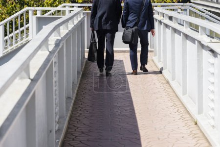 Photo for Two unrecognizable businessman with briefcases walking on a pedestrian bridge - Royalty Free Image