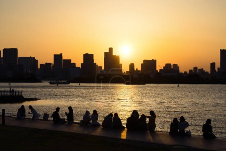 Téléchargez les photos : Vue depuis Odaiba, Tokyo, sur la baie jusqu'à l'horizon de Tokyo au coucher du soleil avec des silhouettes de personnes méconnaissables au premier plan - en image libre de droit