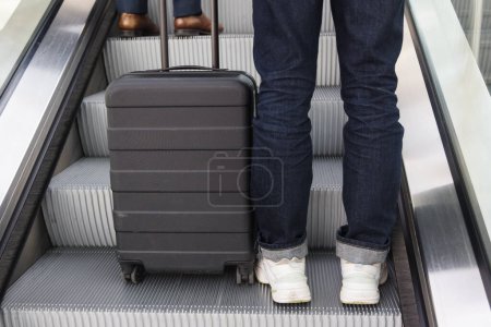 Téléchargez les photos : Jambes d'une personne avec une valise à roues sur un escalier roulant - en image libre de droit