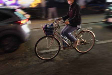 Téléchargez les photos : Image avec effet flou de mouvement d'un homme avec vélo dans la circulation de la ville la nuit - en image libre de droit