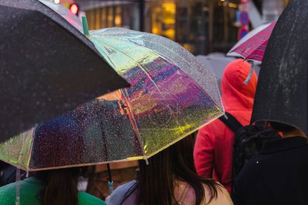 Téléchargez les photos : Photo de personnes avec des parasols qui attendent dans une rue de la ville pluvieuse - en image libre de droit