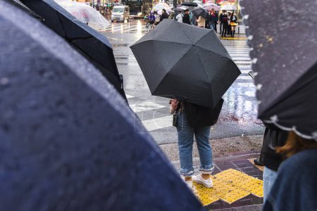 Foto de Foto de personas con sombrillas esperando en una calle de la ciudad lluviosa - Imagen libre de derechos