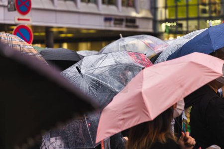 Téléchargez les photos : Photo de personnes avec des parasols qui attendent dans une rue de la ville pluvieuse - en image libre de droit