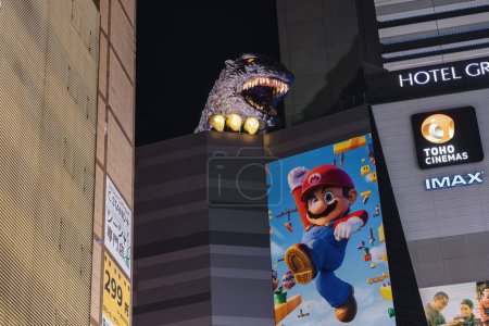 Foto de Tokio, Japón - 09 de abril de 2023: Godzilla escultura en un edificio de los Cines Toho en Kabukicho, Shinjuku, Tokio, por la noche. Kabukicho es un distrito de entretenimiento en Shinjuku. La famosa zona de Kabukicho tiene muchos cines - Imagen libre de derechos