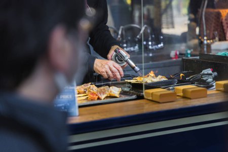 Téléchargez les photos : Un chef dans une cuisine de rue sur le célèbre marché aux poissons Tsukiji à Tokyo, au Japon, préparant des fruits de mer à l'aide d'un brûleur Bunsen - en image libre de droit