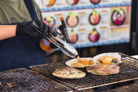 Téléchargez les photos : Un chef dans une cuisine de rue sur le célèbre marché aux poissons Tsukiji à Tokyo, Japon, prépare des fruits de mer à l'aide d'un brûleur Bunsen - en image libre de droit
