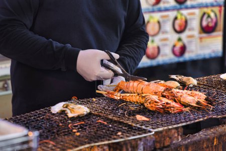 Téléchargez les photos : Un chef dans une cuisine de rue sur le célèbre marché aux poissons Tsukiji à Tokyo, Japon, prépare un homard avec des ciseaux - en image libre de droit