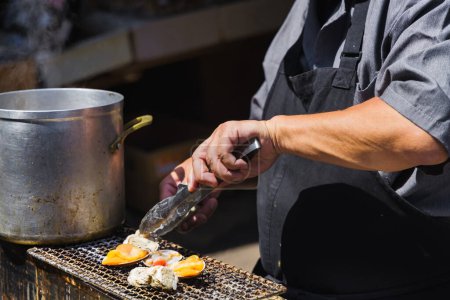 Téléchargez les photos : Un chef dans une cuisine de rue sur le célèbre marché aux poissons Tsukiji à Tokyo, au Japon, préparant des fruits de mer sur un gril - en image libre de droit