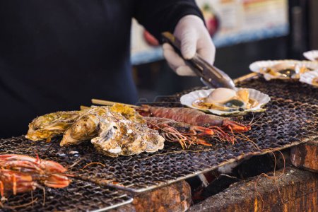 Téléchargez les photos : Un chef dans une cuisine de rue sur le célèbre marché aux poissons Tsukiji à Tokyo, au Japon, préparant des fruits de mer sur un gril - en image libre de droit