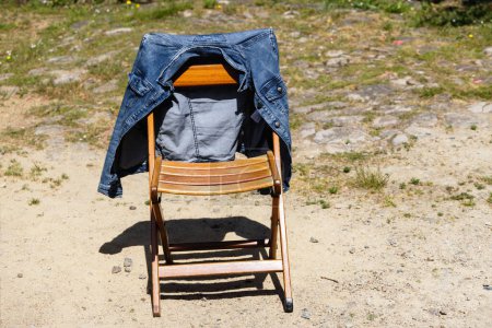 Téléchargez les photos : Photo d'une chaise pliante en bois se tient dans le jardin et une veste en denim pend dessus - en image libre de droit
