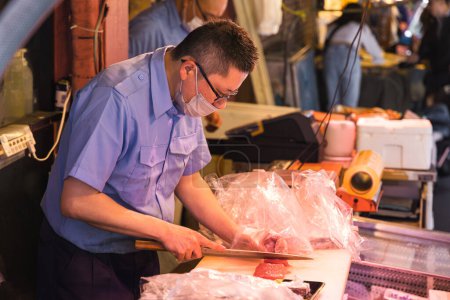 Téléchargez les photos : Tokyo, Japon - 12 avril 2023 : homme non identifié préparant du saumon sur le marché aux poissons de Tsukiji. C'est une attraction touristique majeure. Avant 2018, c'était le plus grand marché de gros de poisson au monde - en image libre de droit