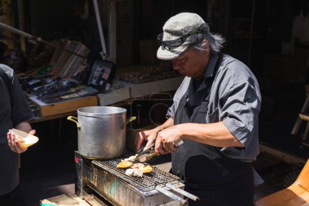 Téléchargez les photos : Tokyo, Japon - 12 avril 2023 : fruits de mer grillés au marché aux poissons de Tsukiji avec des personnes non identifiées. C'est une attraction touristique majeure. Avant 2018, c'était le plus grand marché de gros de poisson au monde - en image libre de droit
