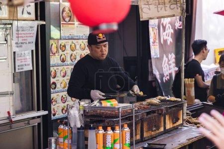 Téléchargez les photos : Tokyo, Japon - 12 avril 2023 : étal de nourriture de rue sur le marché aux poissons de Tsukiji avec des personnes non identifiées. C'est une attraction touristique majeure. Avant 2018, c'était le plus grand marché de gros de poisson au monde - en image libre de droit