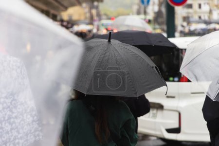 Téléchargez les photos : Photo d'une foule de personnes avec des parasols marchant dans la ville sous la pluie - en image libre de droit