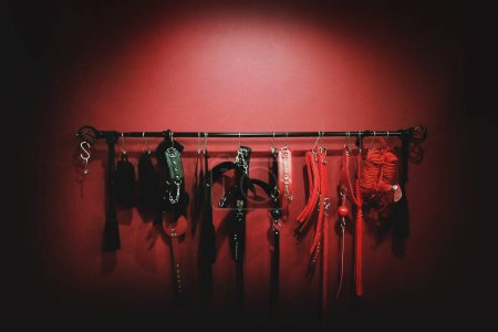 Foto de Whips for BDSM on red background in darkside. Accessory for sexual games. - Imagen libre de derechos