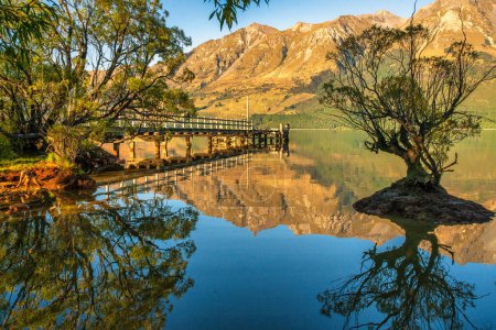 Téléchargez les photos : Réflexions à la surface d'un lac calme Wakatipu des arbres des montagnes et du quai - en image libre de droit