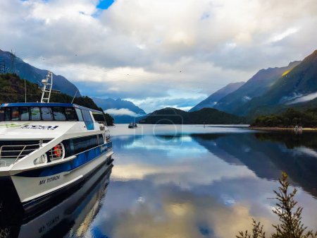 Téléchargez les photos : Superbes reflets cristallins à la surface du lac Manapouri avec le navire de croisière n le quai commercial - en image libre de droit