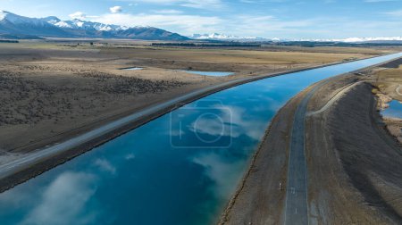 Téléchargez les photos : Vue aérienne du canal du projet hydroélectrique Pukaki dans le Twizel rural fonctionnant en parallèle avec la chaîne de montagnes Ben Ohau maintenant plafonnée - en image libre de droit