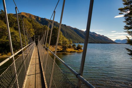 Suspension swing bridge over a remote alpine lake surrounded by forest