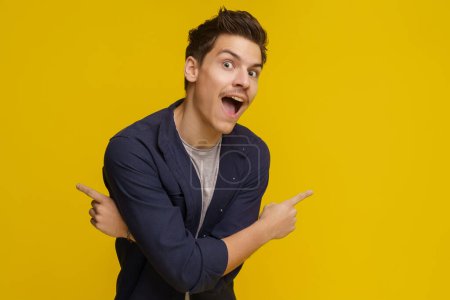 Photo for Young man stands on yellow background with surprised look, pointing in two opposite directions with his crossed hands. Image has ample copy space for text or other design elements. High quality photo - Royalty Free Image