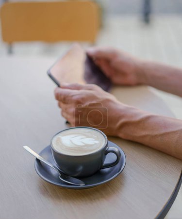 Photo for Coffee and technology in a city cafe setting. In the frame, a steaming cup of coffee takes center stage, showcasing the rich aroma and inviting warmth of the beverage. . High quality photo - Royalty Free Image