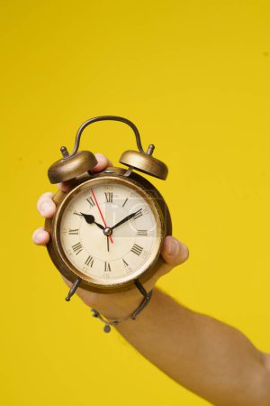 Photo for Alarm clock held in mans hand, isolated on vibrant yellow background. image represents importance of time, waking up early, and managing ones schedule effectively. . High quality photo - Royalty Free Image