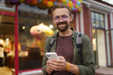 Photo for Happy man texting message while standing in front of shop window adorned with colorful air balloons. Scene filled with joy and positivity, capturing essence of modern communication in urban - Royalty Free Image