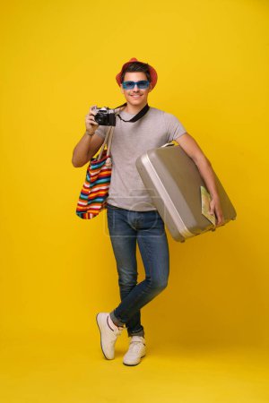 Foto de Un hombre parado al aire libre sosteniendo una maleta en una mano y una cámara en la otra, preparándose para viajar o capturar momentos en la película. - Imagen libre de derechos