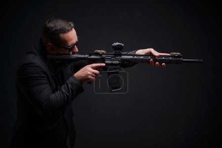Photo for A man dressed in a suit is holding a rifle in his hands, looking focused and determined. He appears to be in a serious and intense mindset. - Royalty Free Image