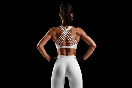 Mujer fitness mostrando los músculos de la espalda sobre fondo negro. Atlético chica vista trasera