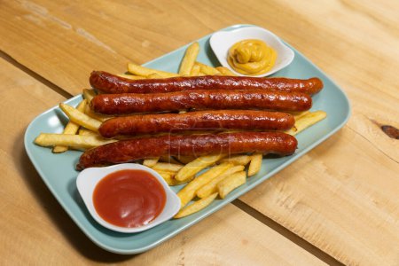 Foto de Embutidos a la parrilla servidos con papas fritas con salsas en un plato - Imagen libre de derechos