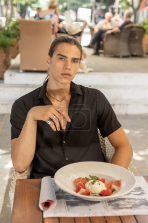 Téléchargez les photos : Jeune homme manger seul dans le restaurant en plein air - en image libre de droit