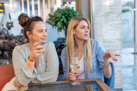 Téléchargez les photos : Joyeuses petites amies buvant du vin dans un restaurant - en image libre de droit