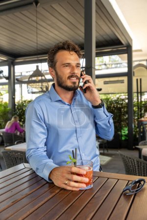 Photo for Handsome man talking on the smartphone in outdoor cocktail bar - Royalty Free Image