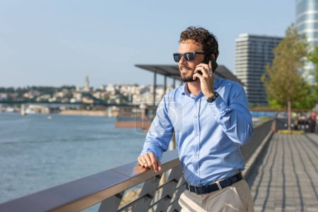 Téléchargez les photos : Jeune homme d'affaires parlant sur le smartphone au bord de la rivière - en image libre de droit
