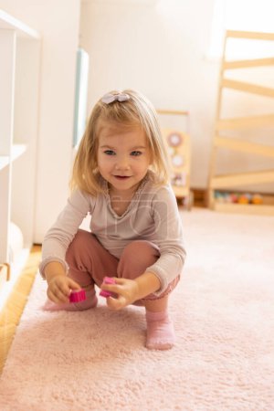Téléchargez les photos : Petite fille jouant seule à la maternelle avec des jouets en bois - en image libre de droit