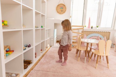 Téléchargez les photos : Petite fille jouant seule à la maternelle avec des jouets en bois - en image libre de droit