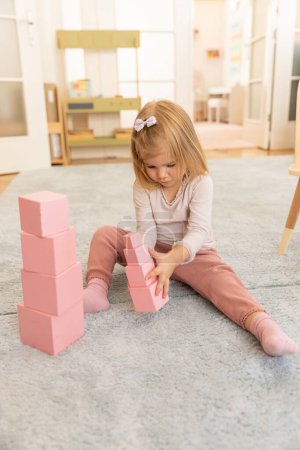 Photo for Small girl playing with pink wooden cubes in the kindergarten - Royalty Free Image