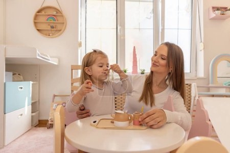 Photo for Young girl playing with her mother with wooden toys, eating, drinking - Royalty Free Image