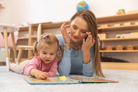 Photo for Mother and toddler daughter lying on the floor reading - Royalty Free Image