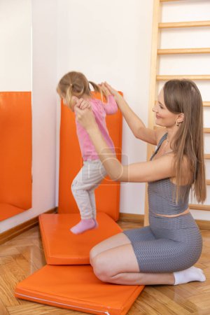 Téléchargez les photos : Jeune femme et la petite fille faisant de l'exercice ensemble dans la salle de gym - en image libre de droit