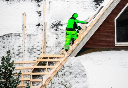 Photo for Workers reroofing or do an overlay for old roof. Building new tilted roof over an old one without removing it. Workers install wood board grid for new roof in the winter to domestic house building. - Royalty Free Image