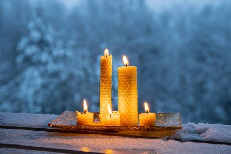 Photo for Set of natural rolled beeswax candles from pressed beeswax honeycomb sheet at home balcony outdoors snowy winter forest on background. Hobby concept. Lot of candles burning with copy space. - Royalty Free Image