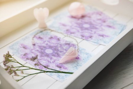 Téléchargez les photos : Deck avec des cartes Angel maison sur plateau blanc à la maison sorcière mise au point sélective sur cristal de quartz rose pendule sur fond est figurine en forme d'ange. - en image libre de droit