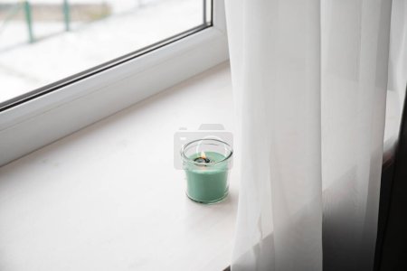 Photo for Candle burning on home window sill, too close to the curtain creating fire hazard. Conceptual image. - Royalty Free Image
