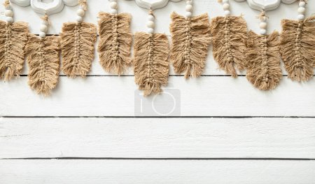 Light brown leaf or feather shape macrame hanging against white wood board background in home room. Lot of copy space, boho background.