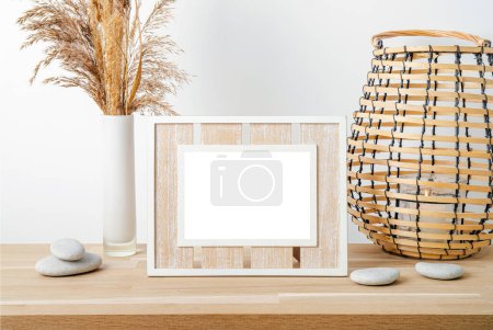 Photo for Minimal natural wood home decor with white empty picture frame, dry reed in vase and round wood lantern with candle burning. Home interior background. - Royalty Free Image